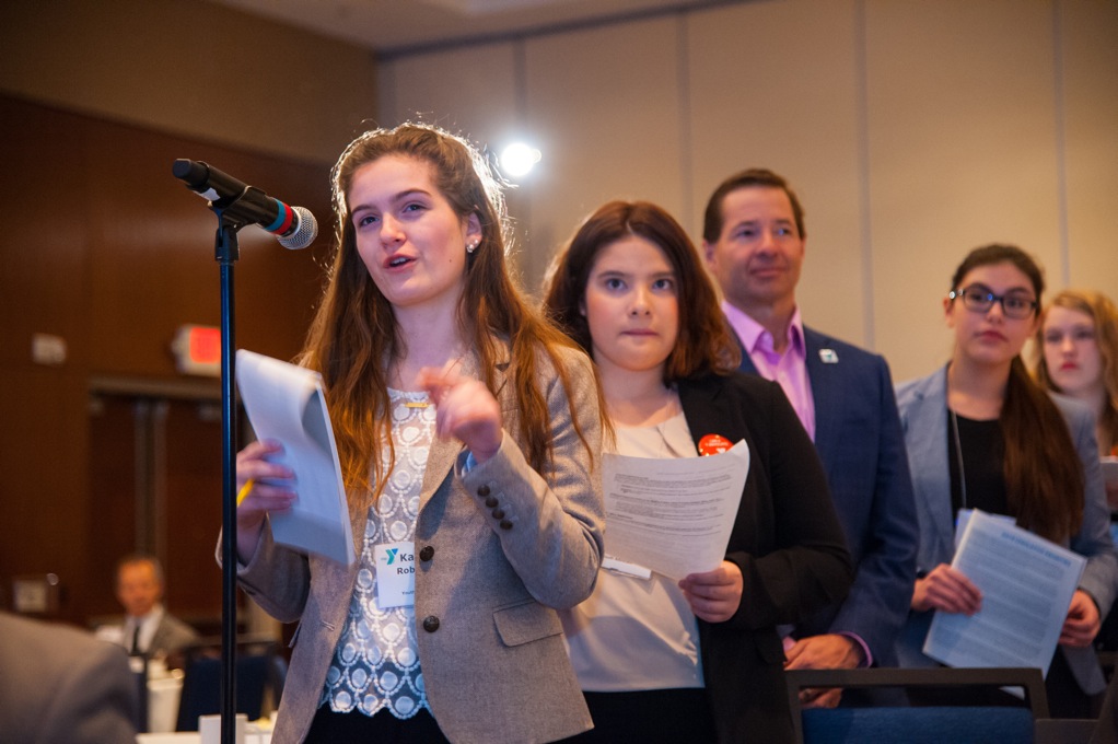Young professionals lined up behind a microphone holding papers Young professionals lined up behind a microphone holding papers