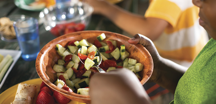 Person scooping tomato cucumber salad out of a wooden bowl Person scooping tomato cucumber salad out of a wooden bowl