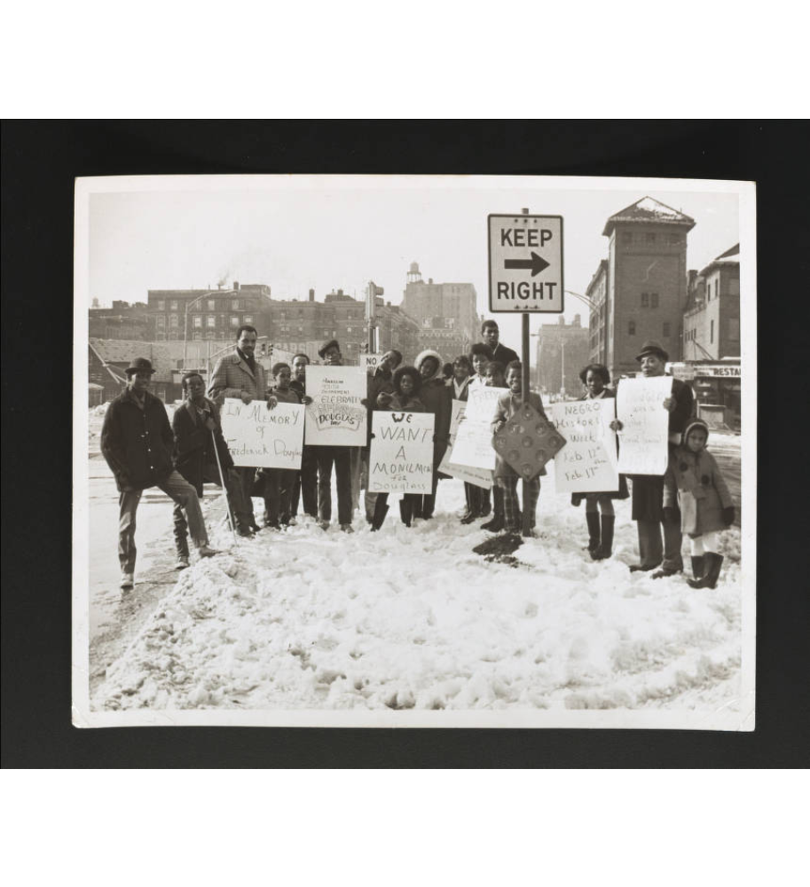 African Americans standing in front of a street sign in Harlem durning the Civil Rights era