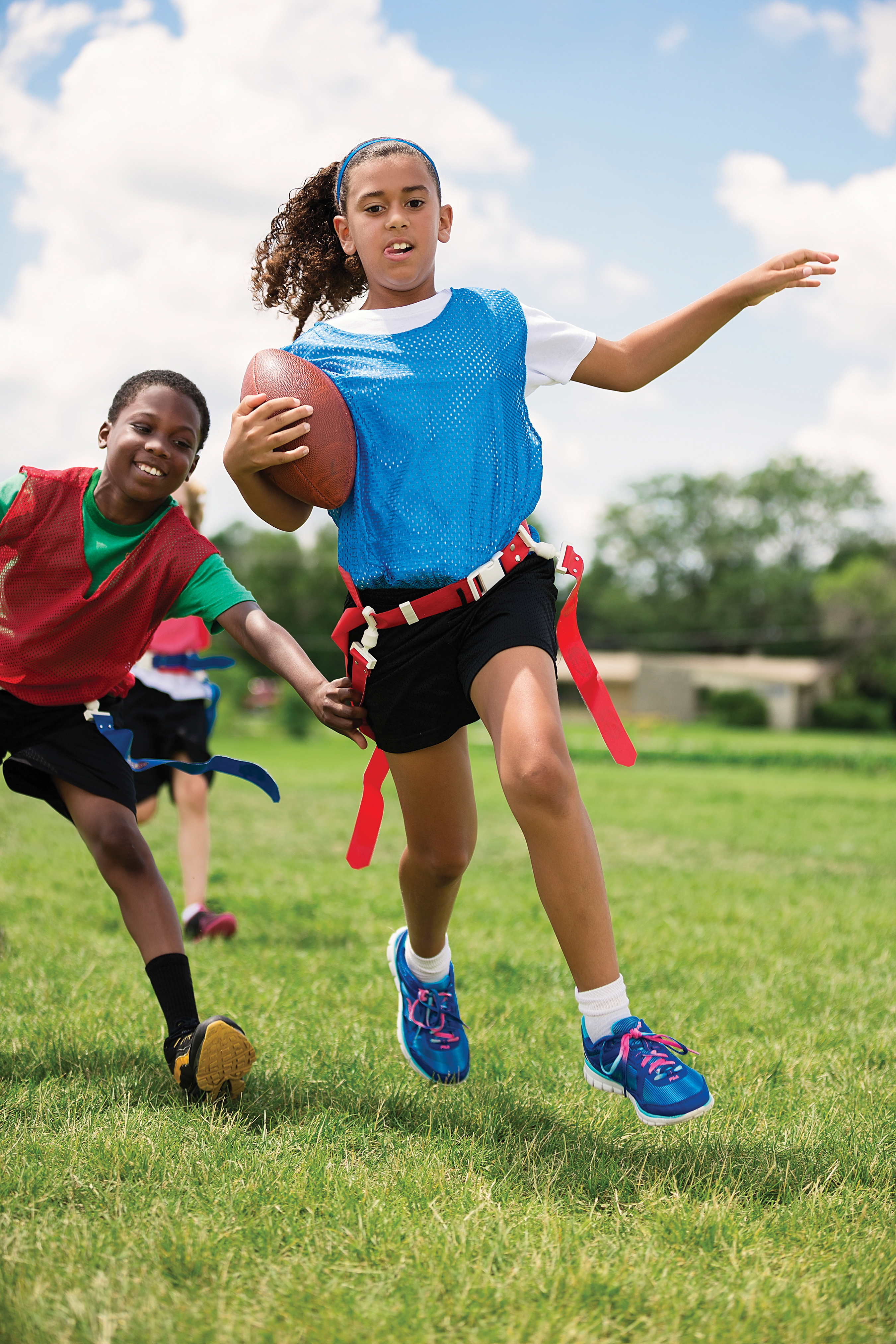 Girl running with football while boy chases during a game of flag football - YMCA Girl running with football while boy chases during a game of flag football - YMCA