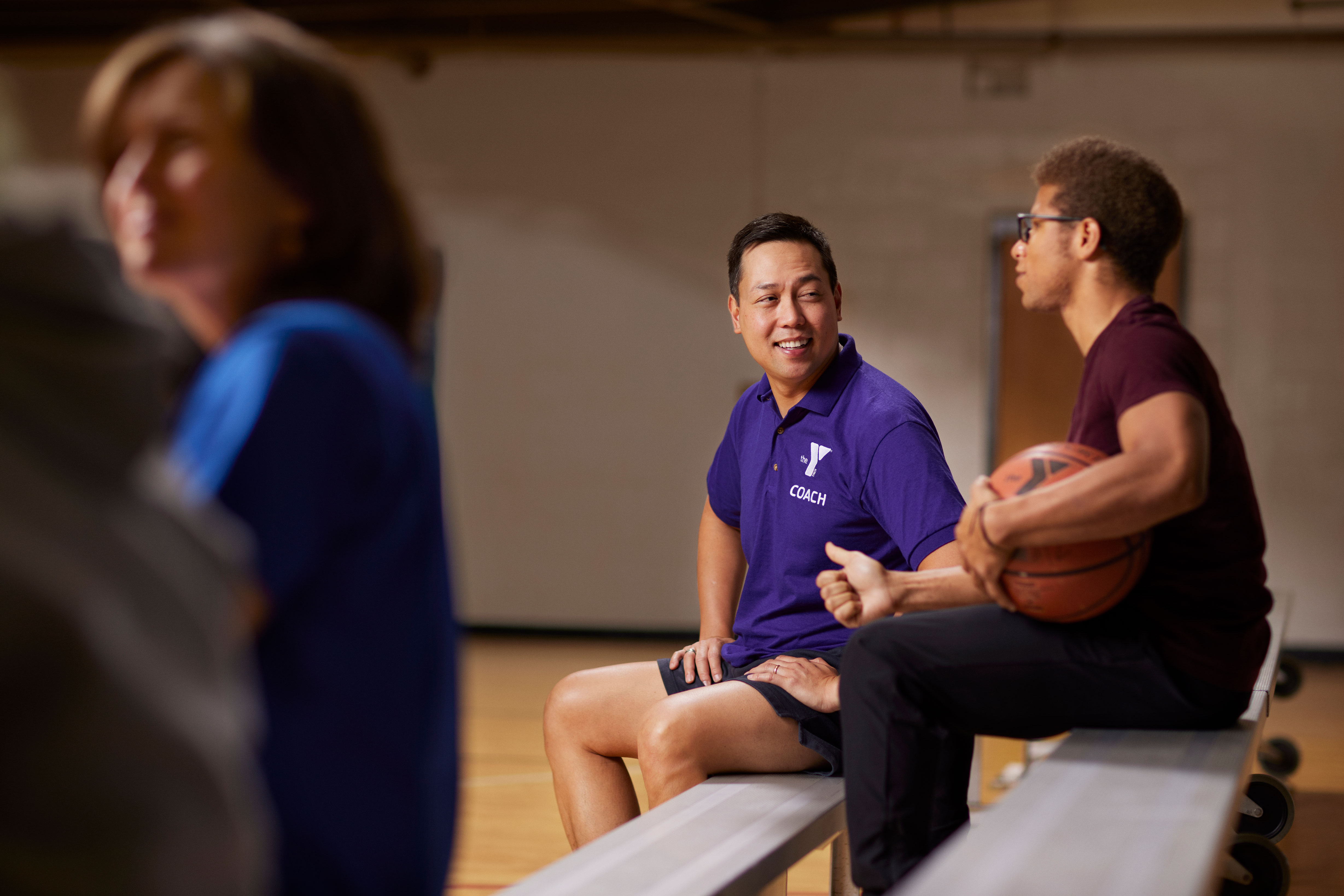 Y coach chatting with male teen on bleachers in gym Y coach chatting with male teen on bleachers in gym