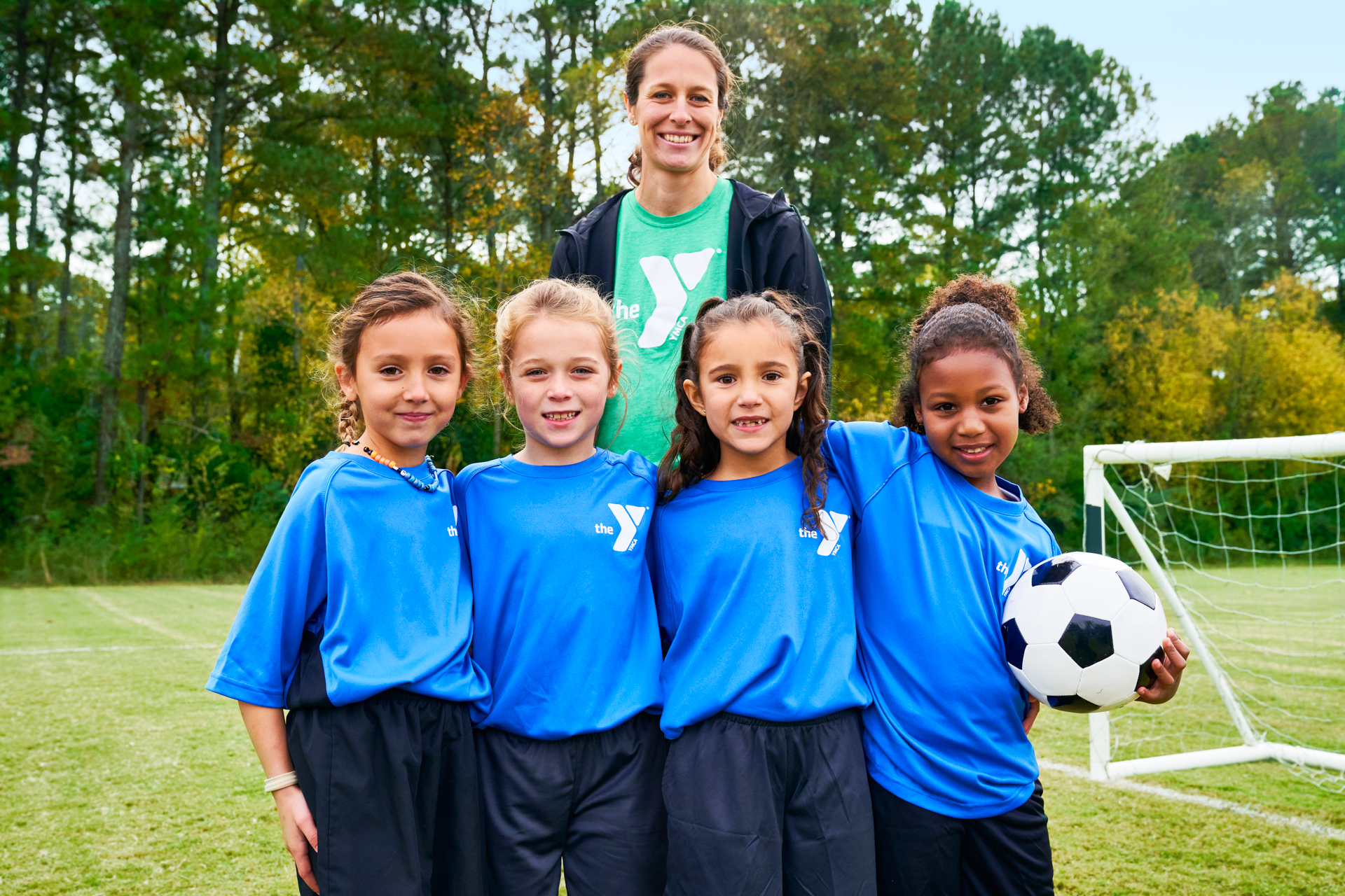 Female Y staff and 4 kids smiling at the camera during soccer practice Female Y staff and 4 kids smiling at the camera during soccer practice