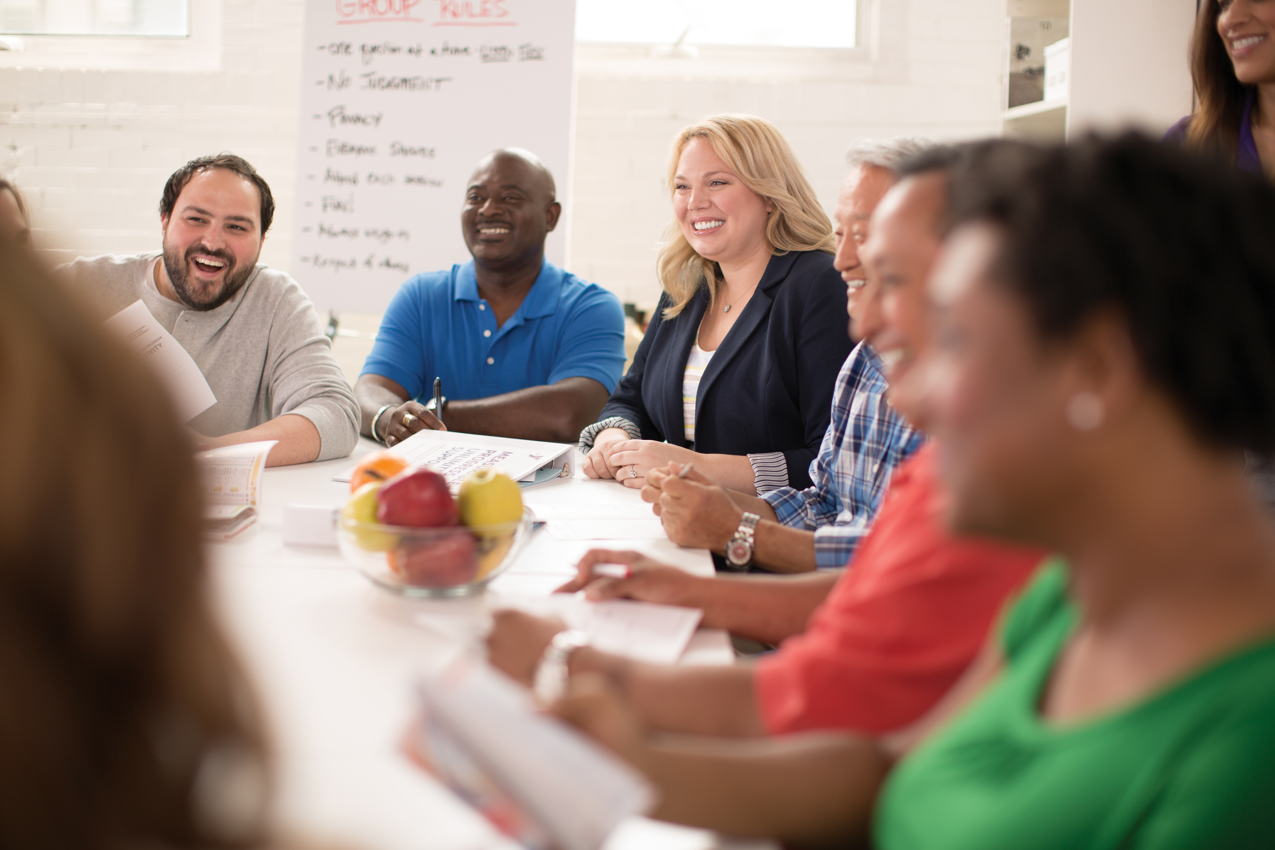 Group of adults sitting around a table with a bowl of fruit talking.