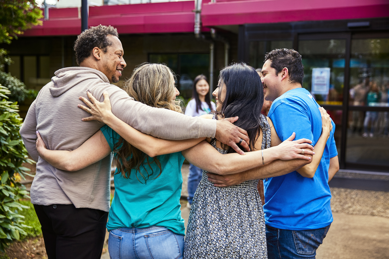 Four adults standing outside with their arms around each other's shoulders