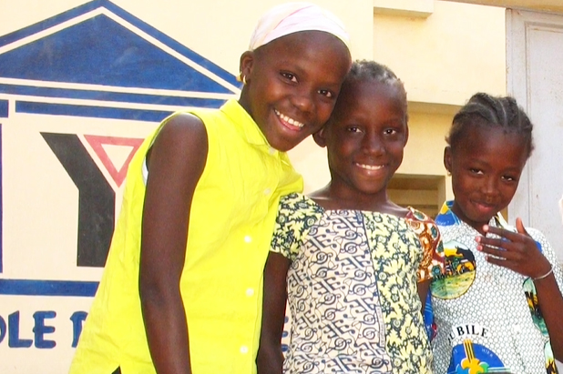 Three young girls smiling in front of an international Y logo 