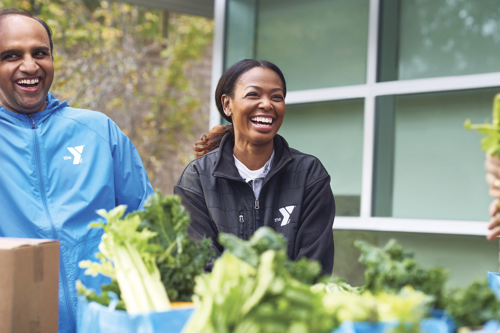 Two Y volunteers bagging vegetables and laughing Two Y volunteers bagging vegetables and laughing