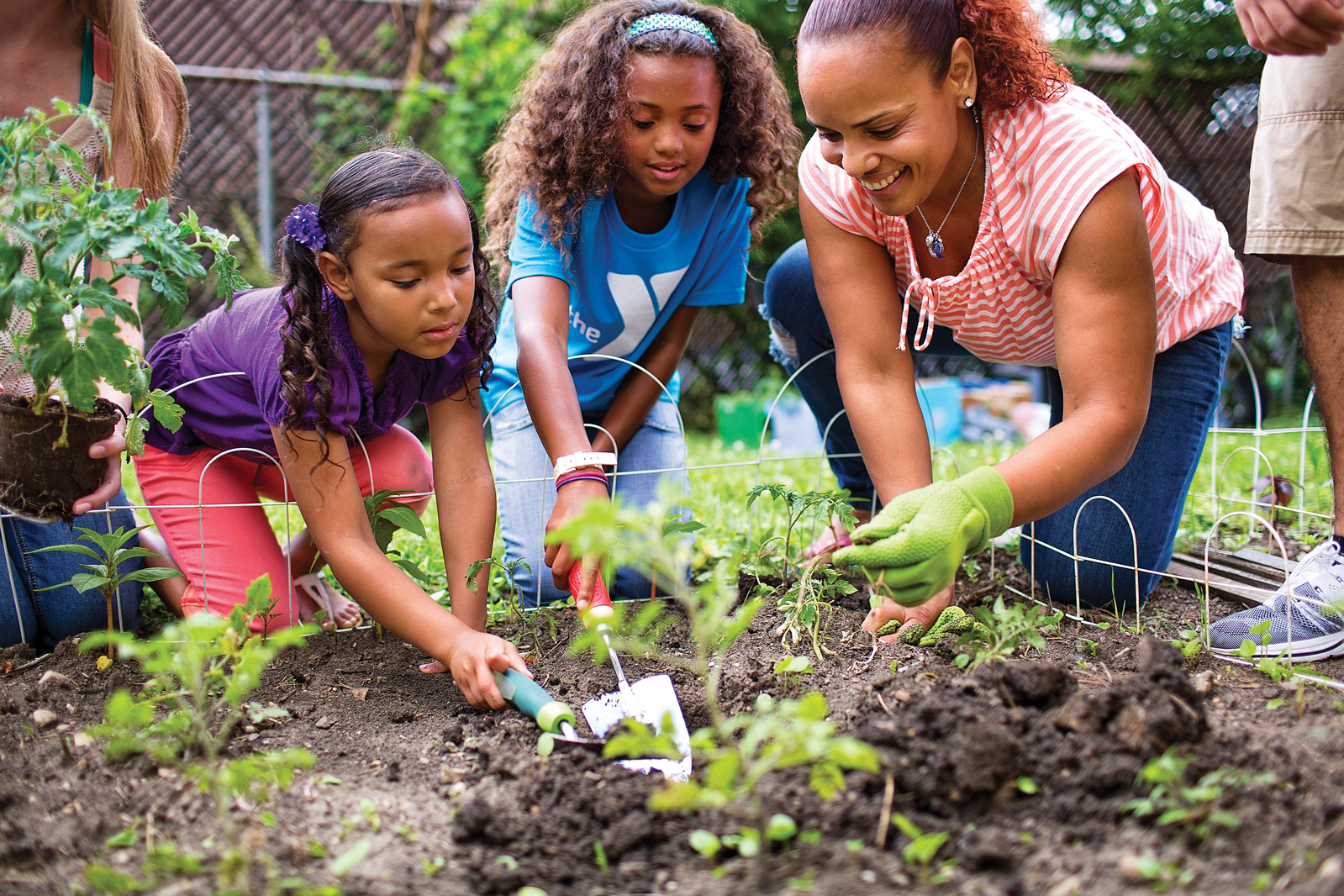 An adult and two youth YMCA members garden outside