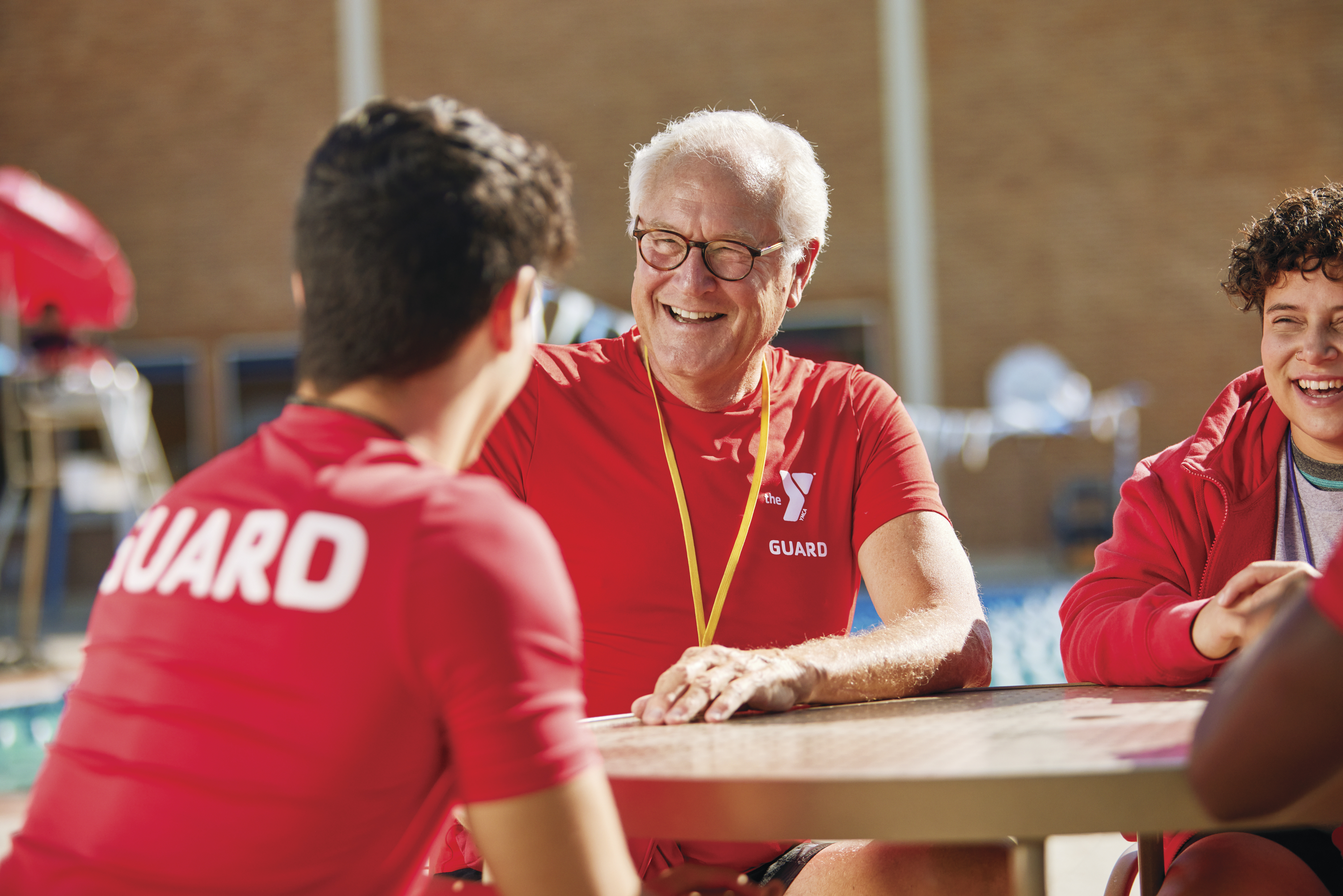 Older adult YMCA lifeguard laughs with younger colleagues 