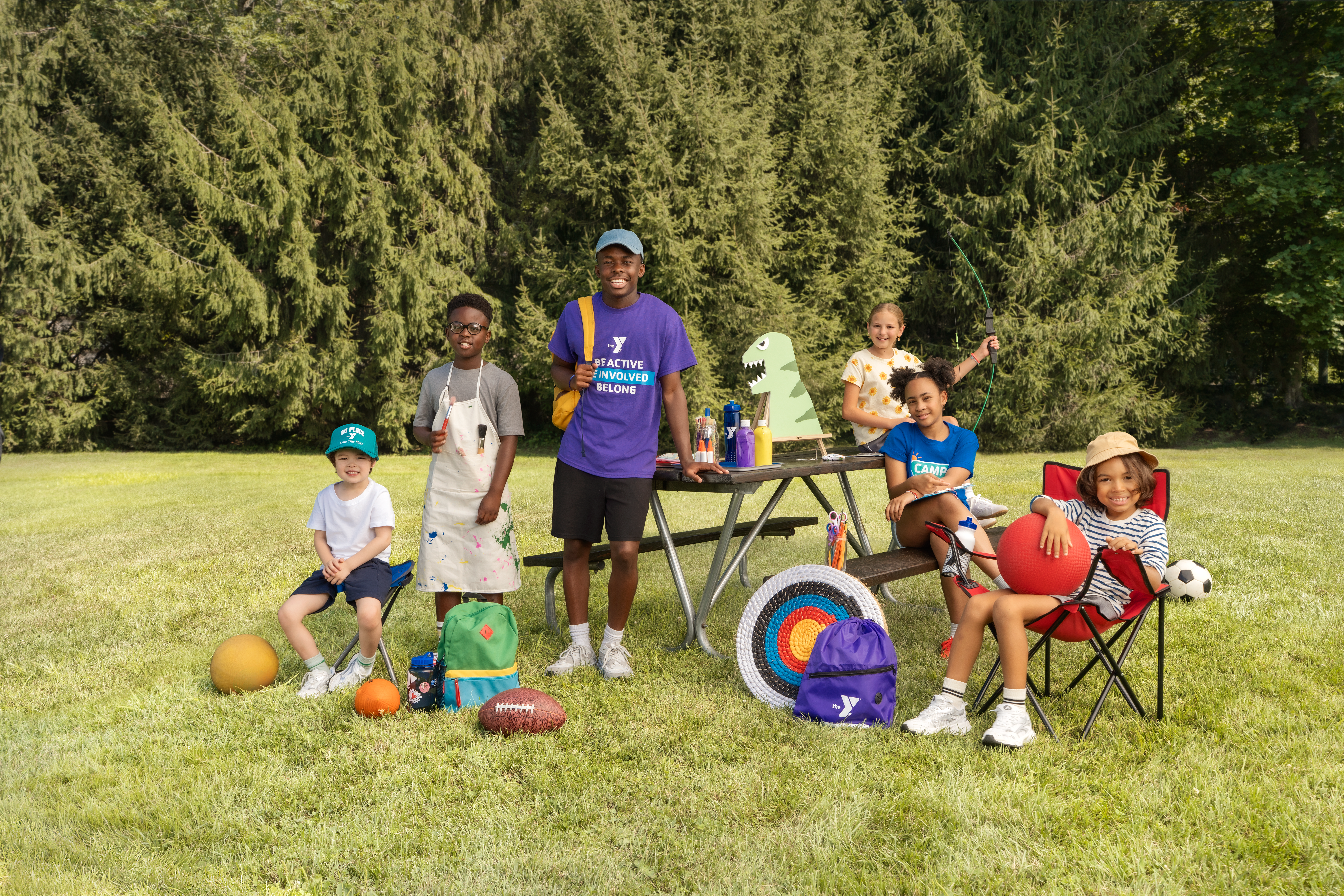 YMCA youth pose with day camp counselor in a field holding sports and activity equipment