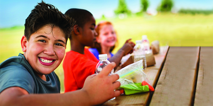 Smiling kids drink water at a picnic table