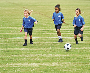 Three young girls in blue jerseys playing soccer