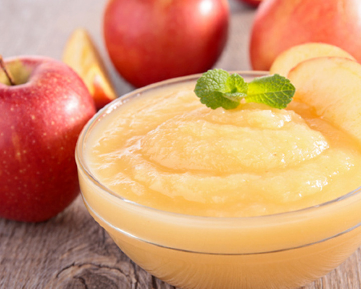 Small bowl of applesauce on wooden table surrounded by whole apples Small bowl of applesauce on wooden table surrounded by whole apples