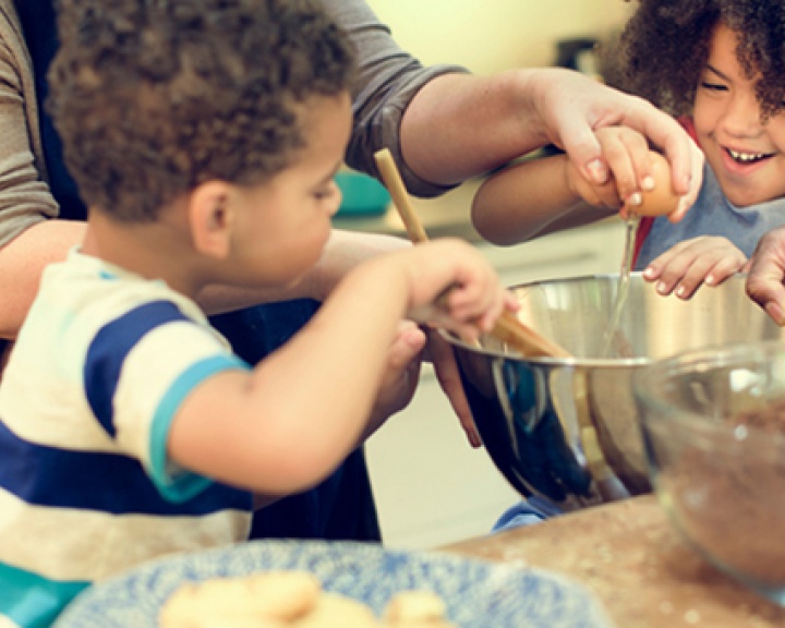 Parents helping children crack eggs into a bowl while baking Parents helping children crack eggs into a bowl while baking
