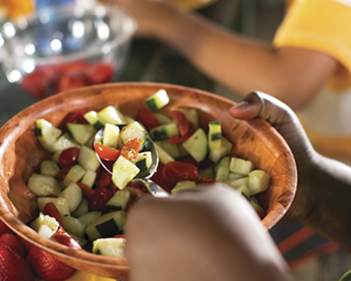 Person scooping tomato cucumber salad out of a wooden bowl Person scooping tomato cucumber salad out of a wooden bowl