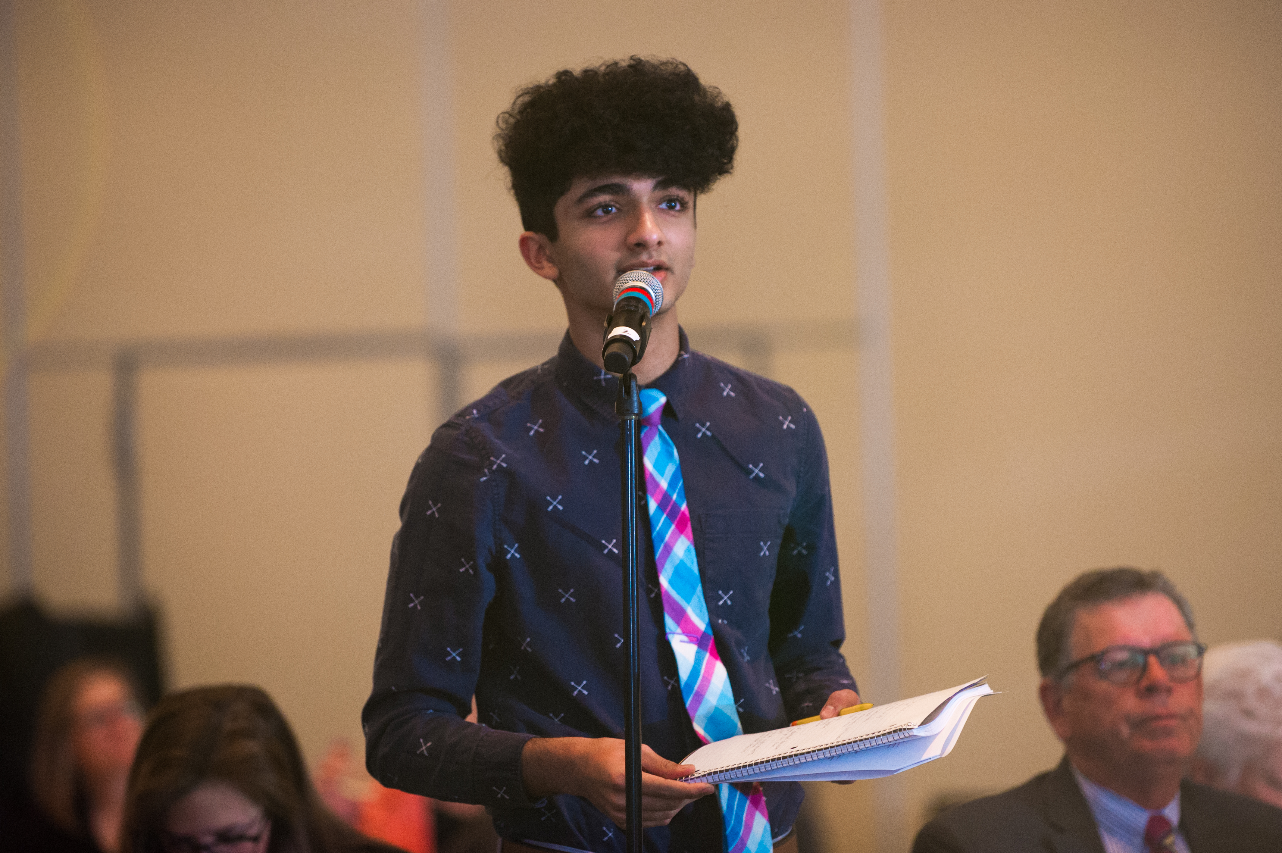 Teen speaking at a microphone with papers in hand Teen speaking at a microphone with papers in hand
