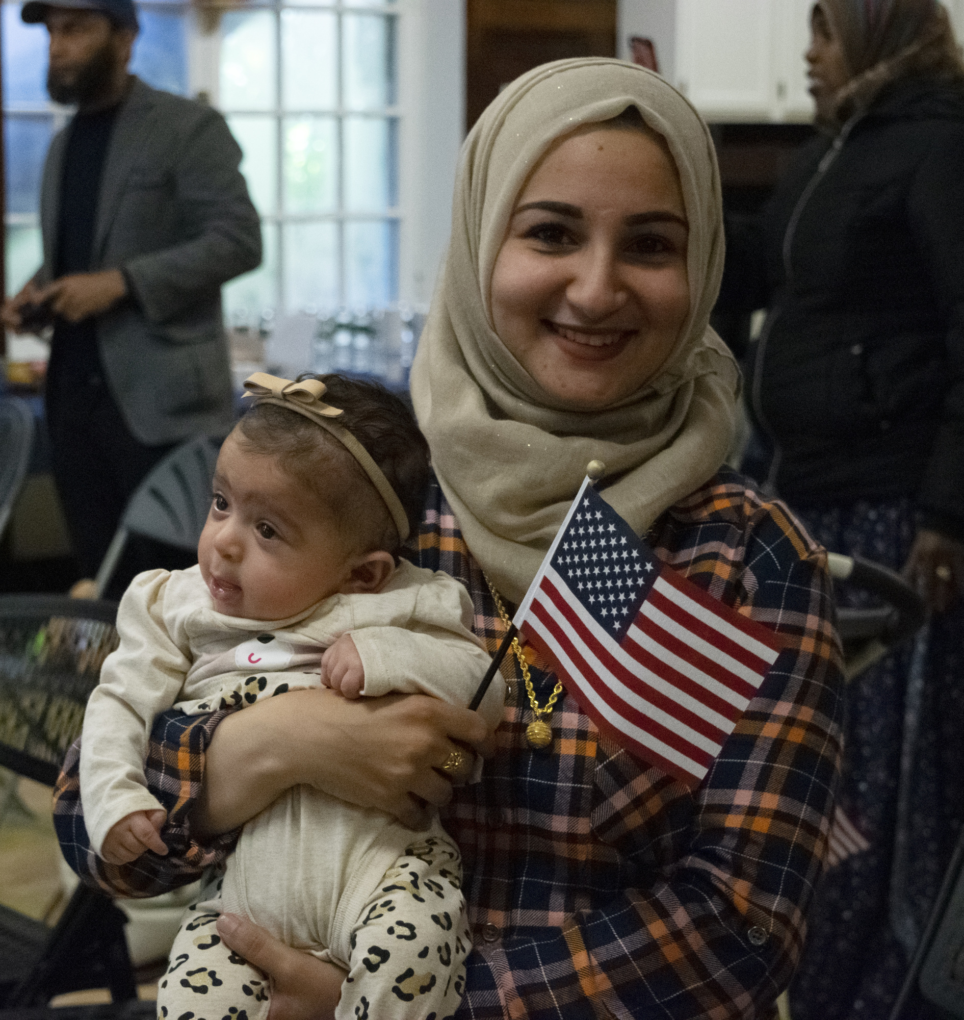 Mother wearing head covering holding her toddler daughter and American flag Mother wearing head covering holding her toddler daughter and American flag