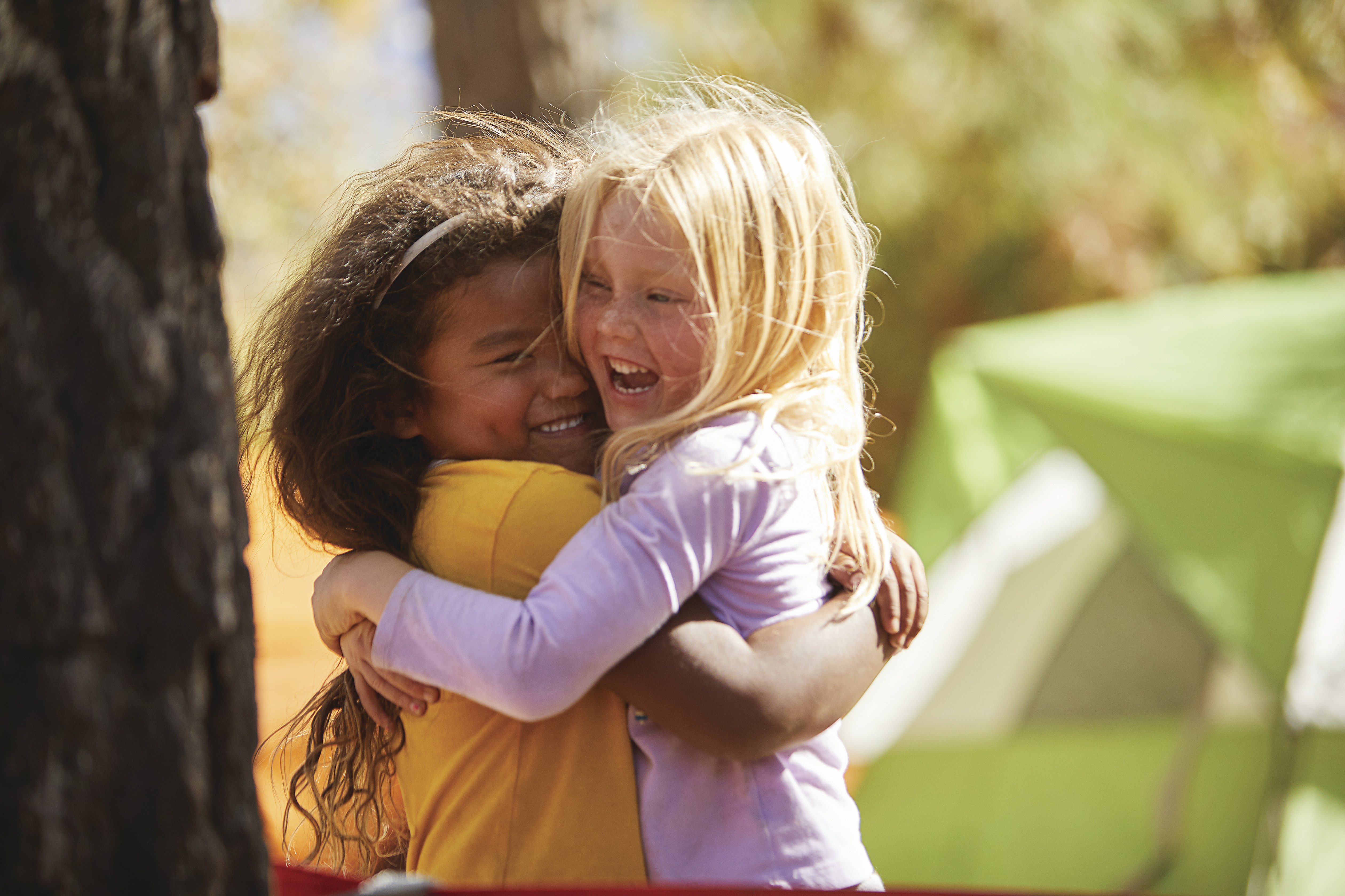 two young friends hugging at overnight camp with tent in the background two young friends hugging at overnight camp with tent in the background