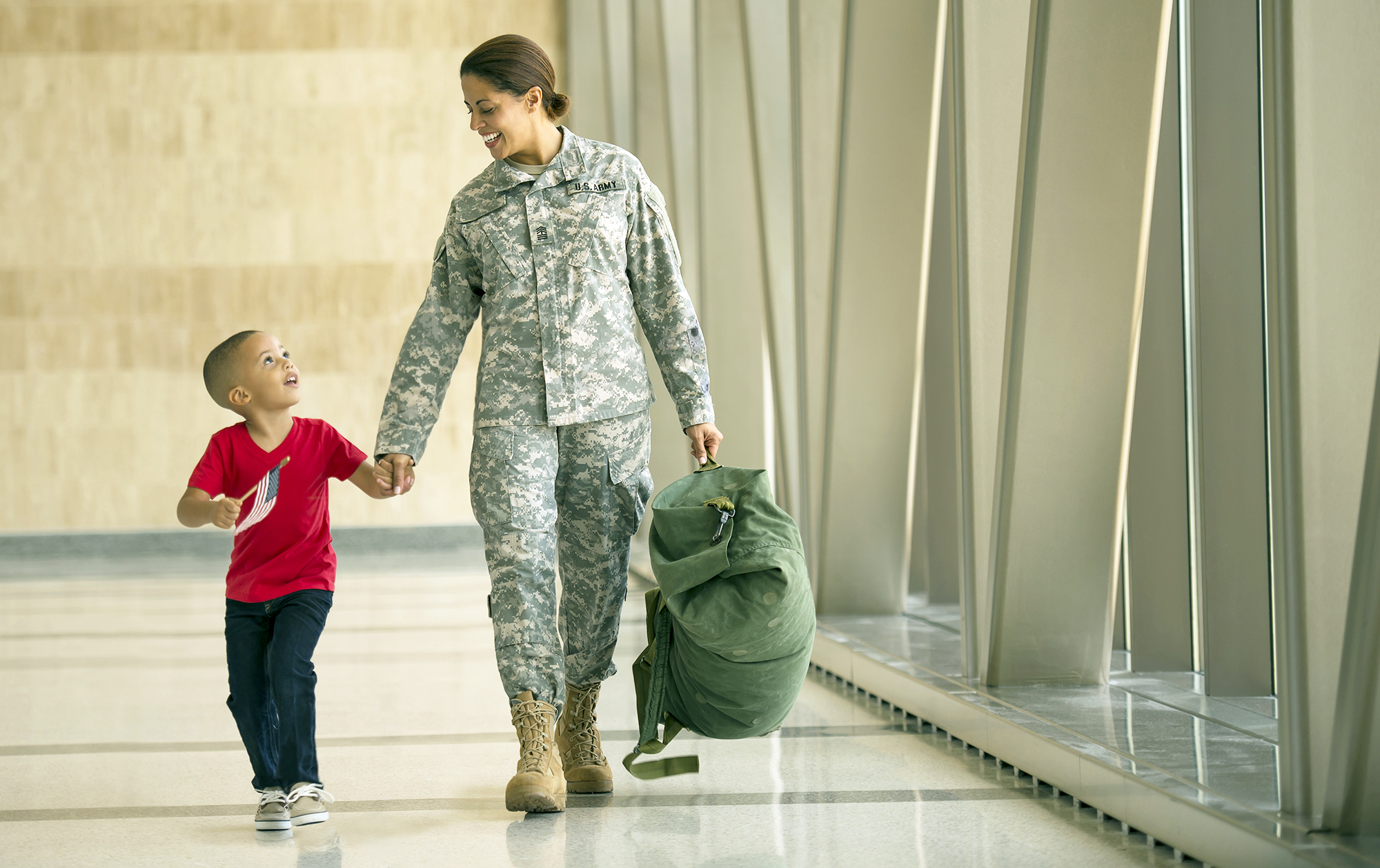 Woman in army fatigues walking through a hallway holding the hand of a young boy Woman in army fatigues walking through a hallway holding the hand of a young boy