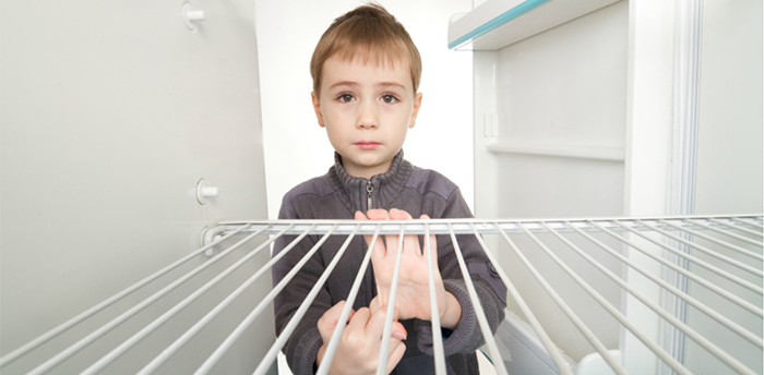 Hungry child standing in front of an empty refrigerator
