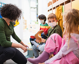 Female childcare employee sitting on the floor with three kids wearing masks.