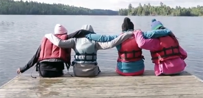 Four children with arms around each other sitting on a dock