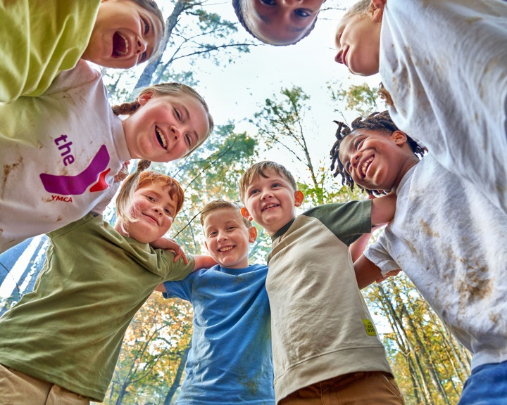 Group of children engaged in a hug while smiling outdoors at Day Camp Group of children engaged in a hug while smiling outdoors at Day Camp