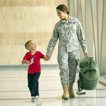 Woman in army fatigues walking through a hallway holding the hand of a young boy Woman in army fatigues walking through a hallway holding the hand of a young boy